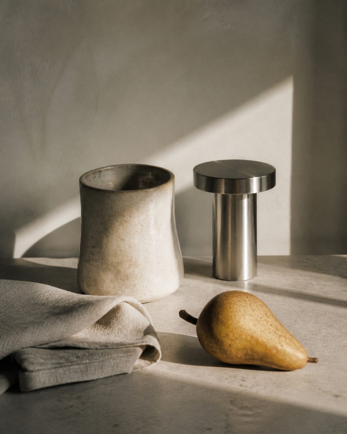 Editorial still-life concept of a ceramic vessel, brushed steel, and pear.